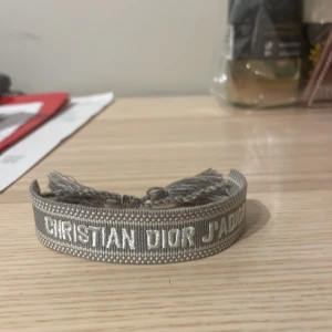 Grått armband från Christian Dior - Säljer detta riktigt feta dior armbandet i ljus grått med tofsar så du kan justera storleken först till kvarn !! Skriv för fler frågor och kan gå ner i pris vid nabb affär !!