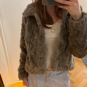 grå pälsjacka - Säljer en mysig pälsjacka med knappar. Jackan har en kortare passform och långa ärmar, perfekt för kyliga dagar. Den är både stilren och trendig, ett måste i garderoben!