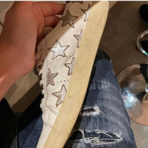 Vita saint laurent sneakers med stjärnor - Snygga vita sneakers dekorerade med silverfärgade stjärnor. Skorna har en klassisk snörning och en bekväm sula. Perfekta för en trendig look.