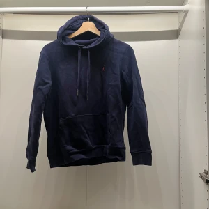 Mörkblå hoodie med broderad logga - Säljer en stilren mörkblå hoodie med en liten broderad logga på bröstet. Tröjan har en klassisk känguruficka och justerbar huva med dragsko. Perfekt för en avslappnad look. Är S men sitter som xs😇