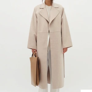 Beige kappa med bälte - Elegant beige kappa med bälte och långa ärmar. Perfekt för en stilren look under kyligare dagar. Kappan har en klassisk design med breda slag och en rak passform.