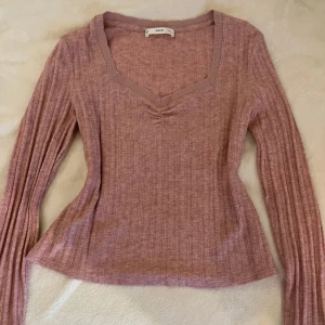 Rosa ribbad tröja från Mango - Säljer en snygg rosa ribbad tröja från MNG. Tröjan har en v-ringad design och långa ärmar, perfekt för en stilren look. Materialet är mjukt och bekvämt, vilket gör den idealisk för både vardag och speciella tillfällen. Storlek L men sitter bra på mig som bär S.