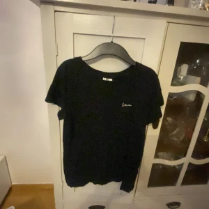 Svart t-shirt från H&M Divided - Säljer en svart t-shirt från H&M Divided med texten 'love' broderad på bröstet. T-shirten är kortärmad och tillverkad i bomull, perfekt för en avslappnad stil.