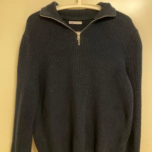 Mörkblå quarter-zip tröja från Zara - Säljer en mörkblå stickad tröja från Zara med dragkedja vid halsen. Tröjan har en klassisk design med långa ärmar och är perfekt för kyligare dagar. 