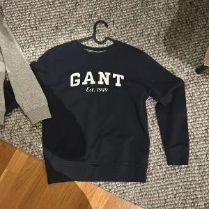 Mörkblå och grå sweatshirt från GANT - Två stilrena sweatshirts från GANT i mörkblått och grått med tryck 'GANT Est. 1949' på bröstet. Perfekta för en avslappnad look med rund hals och långa ärmar. Båda är i storlek 158/164