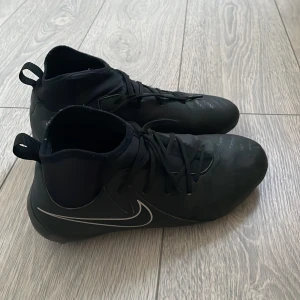 Svarta fotbollsskor från Nike - Snygga svarta fotbollsskor från Nike med snörning och en stilren design. Perfekta för fotbollsplanen med en bekväm passform och bra grepp.