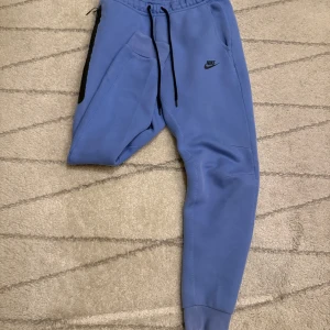 Blå mjukisbyxor från Nike - Snygga blå mjukisbyxor från Nike med svarta detaljer. Byxorna har en bekväm passform med resår och snörning i midjan. Perfekta för en avslappnad stil. Nytt pris 1250