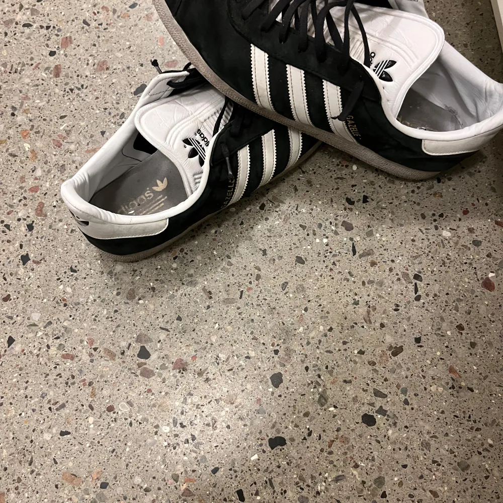 Snygga gazelle sneakers i svart och vitt med klassiska tre ränder på sidan. Skorna har snörning och en bekväm passform, perfekt för vardagsbruk.. Kengät.