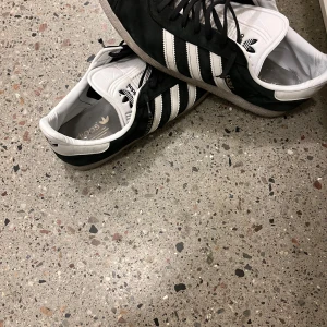 Mocka sneakers  - Snygga gazelle sneakers i svart och vitt med klassiska tre ränder på sidan. Skorna har snörning och en bekväm passform, perfekt för vardagsbruk.