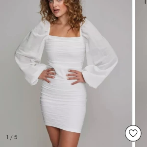 Vit kort klänning med puffärmar - Elegant vit kort klänning med långa puffärmar och en tight passform. Klänningen har en fyrkantig urringning och är tillverkad i ett mjukt material som ger en smickrande silhuett. Skriv om fler bilder 