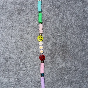 Färgglatt armband med smileys och bokstäver - Ett lekfullt armband med färgglada pärlor i pastellfärger, smiley-ansikten och bokstäver. Armbandet har inslag av grönt, rosa, blått och rött, samt vita pärlor och metalliska detaljer. Perfekt för att ge en glad touch till din stil! Skriv till mig vad ni vill ha för namn på armbandet