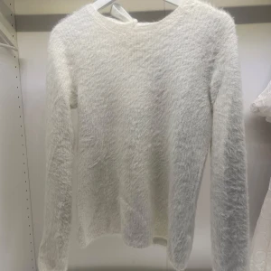 Vit fluffig tröja med knyt i ryggen - Mysig vit tröja med fluffig textur och knytning i ryggen. Tröjan har en fin design och långa ärmar, perfekt för kyligare dagar. Kolla gärna in det andra jag säljer!💘