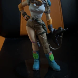 Actionfigur med futuristisk design - En detaljerad actionfigur med futuristisk design. Figuren har en vit topp, beige shorts och blå stövlar. Den är utrustad med skyddsglasögon och håller ett vapen. Perfekt för samlare eller som dekoration.