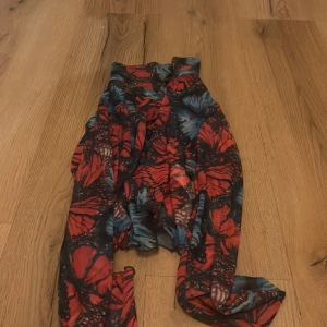 Flerfärgad klänning från FB Sister - Snygg klänning från FB Sister i en färgglad design med fjärilsmönster i rött och blått. Klänningen har knappar framtill och är perfekt för dig som vill sticka ut. Den är tillverkad i ett lätt och luftigt material.