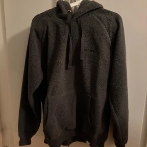 Grå fleece hoodie från Les Deux - Säljer en mysig grå fleece hoodie från Les Deux. Den har en klassisk design med huva och långa ärmar, perfekt för kyliga dagar. Tillverkad av 100% återvunnen polyester. (Aldrig använd)