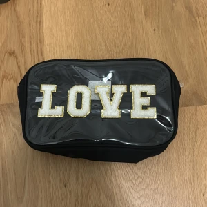 Jättefin svart necessär med texten LOVE - Snygg svart necessär med genomskinlig framsida och texten LOVE i vita teddybokstäver med guldkant från Petite Olivia.  Perfekt för både hudvård och smink💕💕aldrig använd, nyskick💗💗priset går att diskutera💘💘
