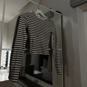 Randig croppad tröja - Säljer en stilren randig tröja med långa ärmar. Tröjan är croppad och har ett klassiskt svartvitt mönster. Perfekt för en avslappnad look.