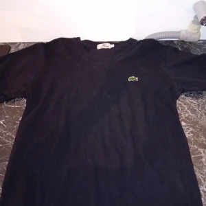 SVART LACOSTE T-SHIRT - Hej!, säljer en svart LACOSTE t-shirt i st.S, den är använde ett få antal gånger och har inga tydliga defekter.