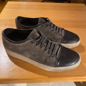 Lanvin Cap Toe - Grå Lanvins. De är köpta här på Plick och användes i ca 3-4 månader. Inga större defekter utan bara sådant som förekommer med tiden. Kolla på bilderna för att bedöma skicket. Har dålig koll på hur man fräschar upp mockan så det går säkert att snygga upp dem en del.  Använts av mig som har storlek 45 i vanliga fall men passar snarare de som har lite större. Alltså för dig som har 45/46. Sitter i en extrasula så att det går att anpassa beroende på person. Kan absolut lösa fler bilder. 