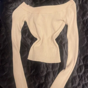 Vit ribbad offshoulder topp från Bik Bok - Säljer en stilren vit ribbad offshoulder topp från Bik Bok. Perfekt för en trendig look med sin åtsittande passform och långa ärmar. Passar utmärkt till både jeans och kjol.