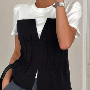 Vit och svart kortärmad topp - Snygg vit och svart topp med korta ärmar. Den har en unik design med en svart del framtill som ger en lager-på-lager-effekt. Perfekt för en stilren look.