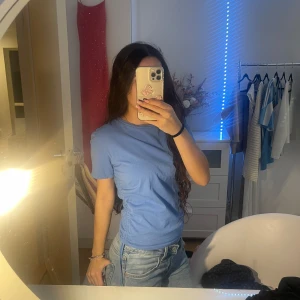 Blå t-shirt från Zara - Snygg blå t-shirt från Zara i en enkel och stilren design. Perfekt för en avslappnad look. T-shirten har korta ärmar och en rund halsringning. Med scrunch på sidorna, går att knyt till en rosett 