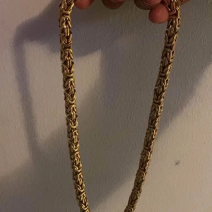 Guldhalsband med kedjedesign från Kejsar - Elegant guldhalsband med en intrikat kedjedesign. Halsbandet har en robust och stilren look, perfekt för att ge en lyxig touch till din outfit. Märkt med 18K för att indikera guldhalten.