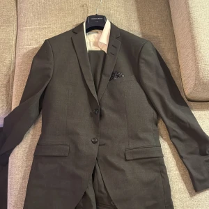 Grå kostym från Tiger of Sweden - Snygg grå kostym från Tiger of Sweden i extra slim passform. Kavajen har två knappar och en stilren design. Perfekt för formella tillfällen.  Skjortan är storlek 39 kavajen 48 byxorna 46 