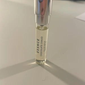 Essence Chocolate Chaud Eau de Parfum - En elegant och kompakt parfymflaska från Essence med doften Chocolate Chaud. Flaskan är genomskinlig med en silverfärgad kork och rymmer 8 ml av denna varma och lockande doft. Perfekt att ha med sig i väskan för en snabb uppfräschning.