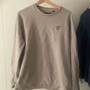 Beige tröja från Lyle & Scott - Säljer en stilren beige tröja från Lyle & Scott med deras ikoniska logga på bröstet. Tröjan har långa ärmar och är tillverkad i mjuk bomull. Perfekt för en avslappnad look.