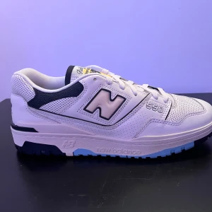 New Balance 550 Rich Paul - Snygga New Balance 550 Rich Paul sneakers i vitt med marinblå detaljer. Skorna har en klassisk design med snörning och perforerade paneler för extra stil. Perfekta för en sportig look.