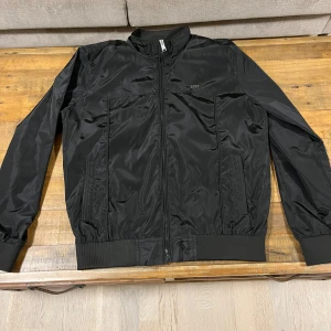 Svart bomberjacka från Boss - Snygg svart bomberjacka från Boss med dragkedja framtill.  Perfekt för en cool och avslappnad stil. Aldrig använd och priset kan diskuteras vid en snabb affär. Säljer pågrund av att den var liten på mig. Passar även i storlek S