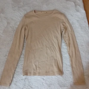 Beige ribbad långärmad tröja - Säljer en stilren beige ribbad tröja med långa ärmar. Perfekt för lager-på-lager under kyligare dagar. Enkel och mångsidig design som passar till det mesta. Hör av dig vid intresse!