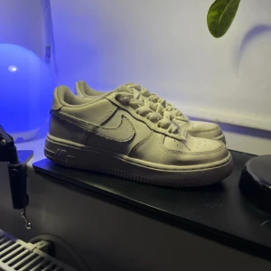 Nike Air Force 1 i vitt - Säljer ett par klassiska Nike Air Force 1 sneakers i vitt. Skorna har en stilren design med snörning och den ikoniska Nike-loggan på sidan. Perfekta för en avslappnad stil. Rätt bra skick och är i strlk 36,5. Tyvärr ingen låda 