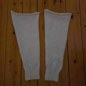 Vita benvärmare - Säljer ett par vita benvärmare i mjukt material. Perfekta för att hålla värmen under kyliga dagar. De har en enkel design med ribbstickade kanter som ger en bra passform.