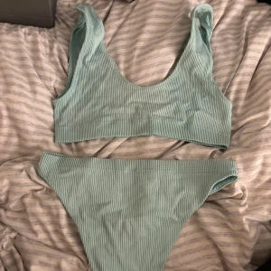 Grön ribbad bikini - Snygg grön ribbad bikini med breda axelband och hög midja. Perfekt för en dag på stranden eller vid poolen. Den ribbade texturen ger en modern och stilren look.