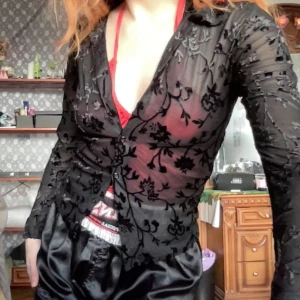 Svart blommig meshskjorta - Svart mjuk meshskjorta med blommigt mönster och transparent design. Blusen har långa ärmar och knappar framtill, vilket ger en elegant look.  Längd: 55cm Bredd: 42cm Ärm: 54cm