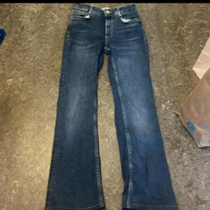 Blå bootcut jeans - Snygga blå bootcut jeans med klassisk femficksdesign och knappgylf. Perfekta för en avslappnad stil med en touch av retro. Passar bra till både sneakers och stövlar.