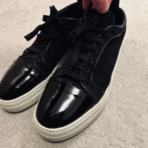 Svarta mocka sneakers med lackdetaljer - svarta mocka sneakers med glansiga lackdetaljer på tån och ovansidan. Det är ett danskt märke, minns inte namnet. Liten skada på höger skon men inget man tänker på (se sista bilden). Nypris 1500kr