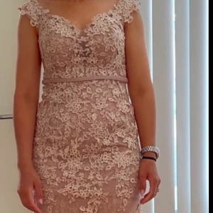 Rosa spetsklänning - Elegant långklänning i rosa med vacker spetsdetaljering. Klänningen har en v-ringad design och är ärmlös, vilket ger en sofistikerad look. Perfekt för speciella tillfällen.