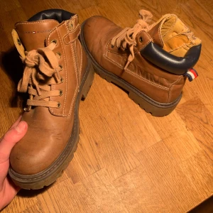 Bruna boots från Tommy Hilfiger - Tjenare! Säljer nu dessa riktigt feta bruna boots från Tommy Hilfiger med snörning och dragkedja. De har en robust sula och mörkblå detaljer vid ankeln. Perfekta för höst och vinter. Bara skorna ingår.