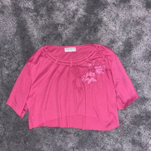 Rosa topp från Reflect - Säljer en söt rosa topp från Reflect med dekorativa blommor och detaljer vid halsringningen. Toppen har korta ärmar och en lös passform, perfekt för vår och sommar.