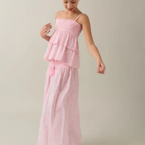 Rosa långkjol med smockdetalj - Pris kan diskuteras Charmig rosa långkjol med smockdetalj i midjan och knytband. Kjolen har en luftig och bekväm passform, perfekt för varma dagar. Den mjuka rosa färgen ger en söt och somrig känsla.