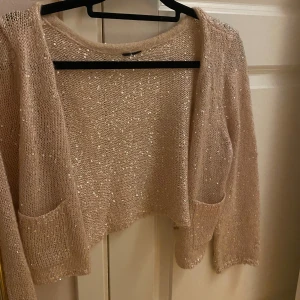 Beige glittrig kofta - Snygg beige kofta med glittriga detaljer. Den är croppad och har 3/4 långa ärmar samt praktiska fickor framtill. Perfekt för att lägga till lite glamour till din outfit. Köpt på sellpy men aldrig använt själv och koftan är i bra skick!❤️