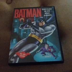 Batman: Berättelsen om den mörke riddaren DVD - DVD med fyra avsnitt av Batman: Berättelsen om den mörke riddaren. Omslaget visar Batman i sin klassiska dräkt med en stadssilhuett i bakgrunden. Texten 'Alla talar svenska!' finns på framsidan.