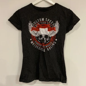 Mörkgrå t-shirt med motorcykeltryck - Cool mörkgrå t-shirt från Primark med ett tryck av dödskallar och vingar samt texten 'Custom Speed Road Race'. Perfekt för en edgy look.
