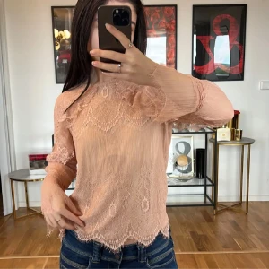 Rosa spetsblus - Säljer en söt rosa blus med spetsdetaljer och volanger. Blusen har långa ärmar och en elegant design som passar perfekt för vår och sommar. Den är tillverkad i ett lätt och luftigt material.