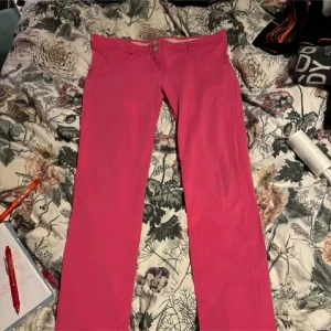Rosa byxor med bootcut - Snygga rosa byxor med bootcut-stil och låg midja. Byxorna har en dragkedja och knapp framtill. Perfekta för att lägga till en färgklick i garderoben!