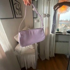 Lila väska  - Säljer denna lila Axel väska. Super fin färg och perfekt till våren och sommaren. Kommer inte till använding längre då den inte är min still. Väskan är knappt använd. Köpte väskan på H&m för länge sedan. Säljer den för 55kr+frakt
