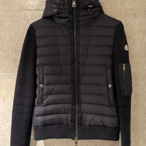 Moncler cardigan - Snygg mörkblå jacka från Moncler med quiltad design och stickade ärmar. Jackan har en huva och dragkedja framtill samt praktiska fickor med knappar. Perfekt för kyligare dagar. Pris är inte hugget i sten! Skriv för fler frågor och bilder! Fraktad dirket🚚📦